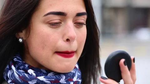Young lady while looking on the mirror make her lips red lipstick on the street. Stock Footage 75582593