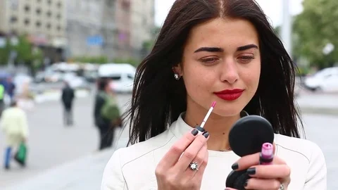 Young lady while looking on the mirror make her lips red lipstick on the street. Stock Footage 75582608