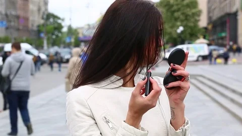 Young lady while looking on the mirror make her lips red lipstick on the street. Stock Footage 75582624