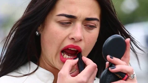 Young lady while looking on the mirror make her lips red lipstick on the street. Stock Footage 75582650