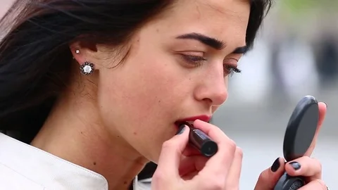 Young lady while looking on the mirror make her lips red lipstick on the street. Stock Footage 75582682