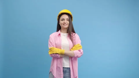 Young lady worker in yellow hard hat and gloves on blue background Stock Footage 243739286