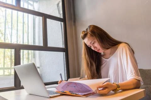 Young lady working on documents and laptop next to window Stock Photos