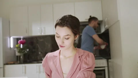 A young lady is working at home and her husband is making house duties on the Stock Footage 156302408
