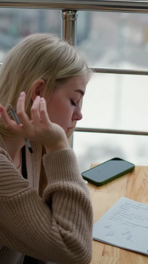 Young lady writes thoughtfully with coffee and phone on table, winter background Video stock 318225648