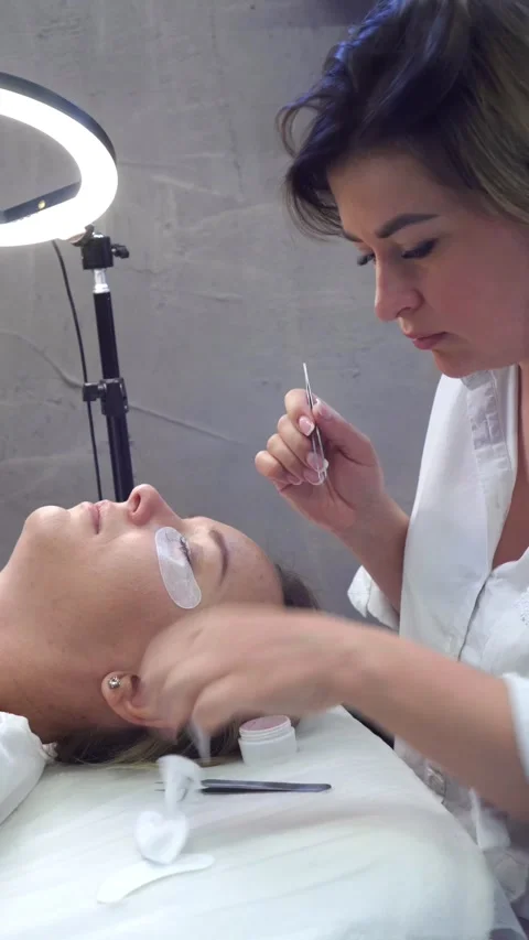 Young lashmaker deleting lashes of client with tweezers and applying degreasing Stock Footage 251635012