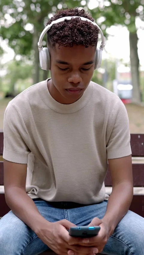 Young latin american boy using mobile phone sitting on bench in city park Stock Footage 235811593