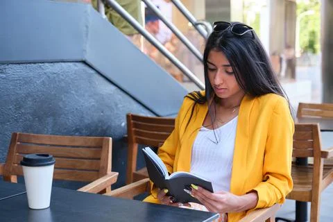 Young latin businesswoman reading a book at a coffee shop. Stock Photos