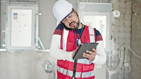 Young latin man builder talking on smartphone using touchpad at constructio.. 스톡 동영상 246988811