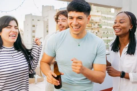 Young latin man dances, looking at camera, gathered with friends on terrace Stock Photos