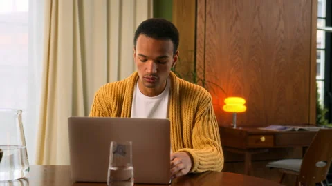 Young Latin man sits at table working at laptop at home Stock Footage 267674699
