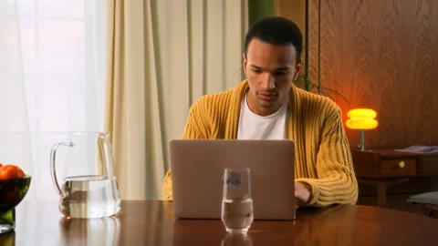 Young Latin man sits at table working at laptop at home Stock Footage 267675465