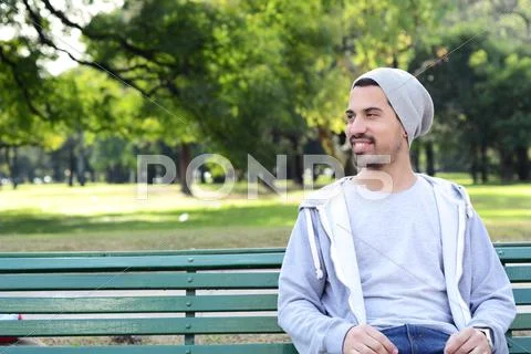 Young Latin Man Sitting On Park Bench.