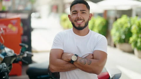 Young latin man standing with arms crossed gesture by motorbike at street Video stock 231508191