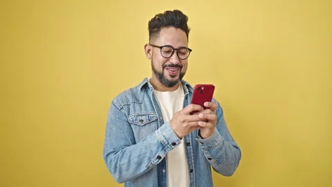 Young latin man using smartphone smiling over isolated yellow background Stock Footage 245048633