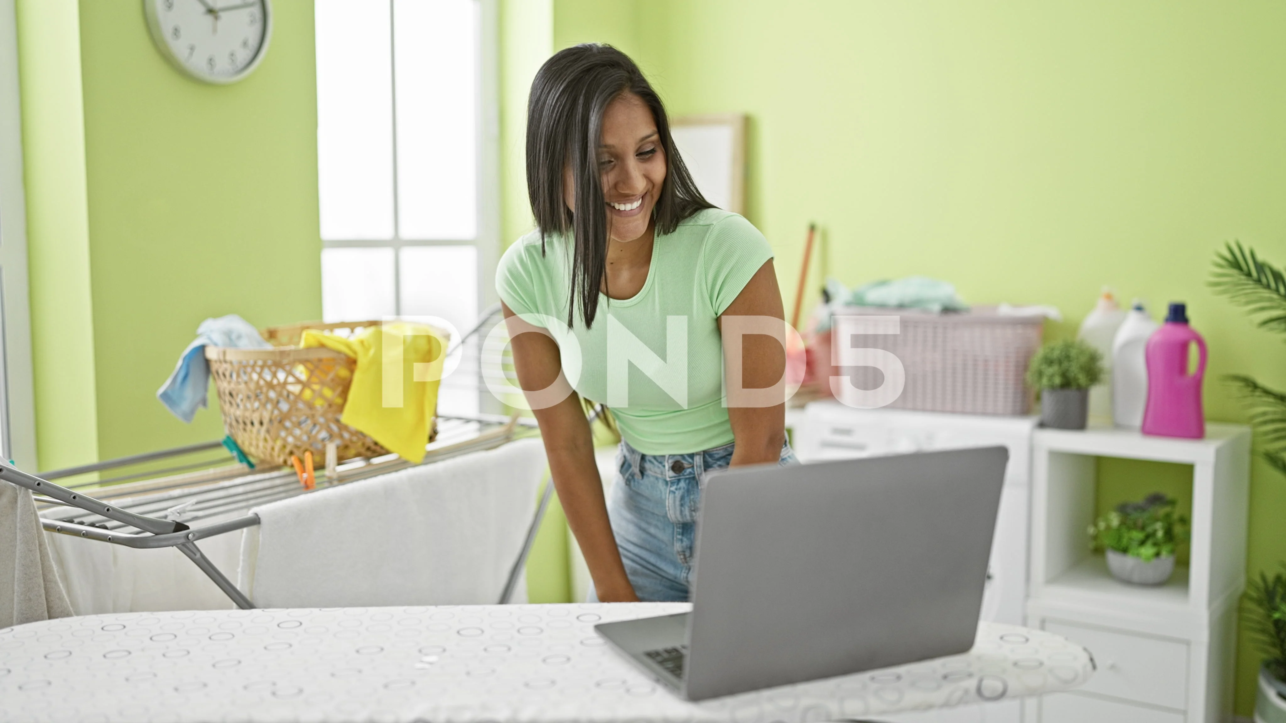 Young latin woman having video call hanging clothes on clothesline at  laund..