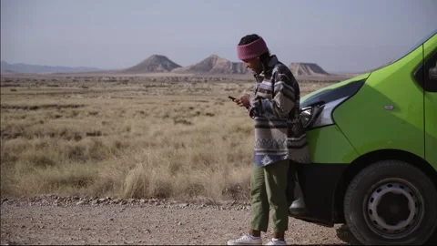 Young latina girl using cell phone leaning bumper camper travels alone on road Stock Footage 249394149