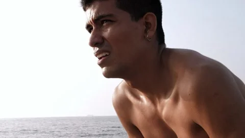 Young latino man catches his breath after finishing running by the sea Stock Footage 256418341