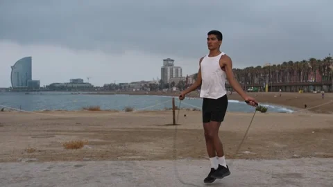 Young latino man exercising jumping the rope during sunrise by the beach Stock Footage 256437375