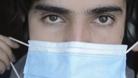 Young latino man looking at camera, and smiling while put on a medical face mask Stock Footage 146199515