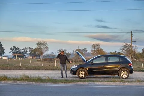 Young Latino man talking on a mobile phone in front of his car broken down .. 스톡 사진