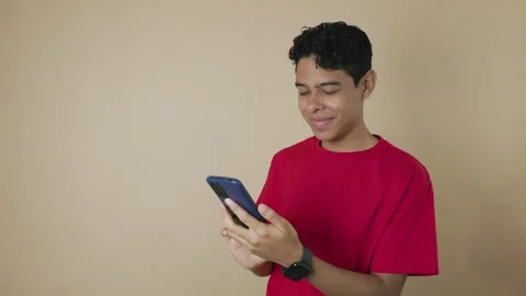 Young Latino man using his cell phone on a light brown background Stock Footage 315062045