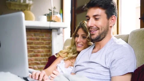 Young laughing couple using laptop while sitting on couch in apartment. Stock Footage 74728597