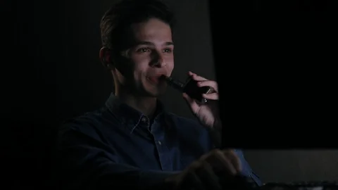 Young laughing man vaping in front of computer at home in dark room Stock Footage 99051116