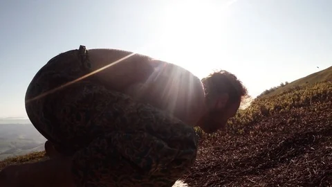 A young lean Yogi is trying to make the postures of Hasta Bhudzhasana in the sun Stock Footage 77781479