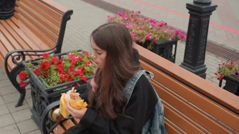 Young learner enjoying snack in vibrant urban surroundings during midday. Casual 스톡 동영상 329890253