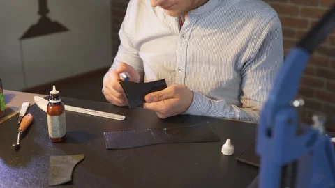 Young leather craftsman creates a DIY product. Workshop owner works in workplace Vidéo 130145875