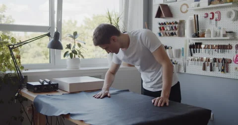 Young leather worker examining large leather piece on a table in workshop Stock Footage 144894307