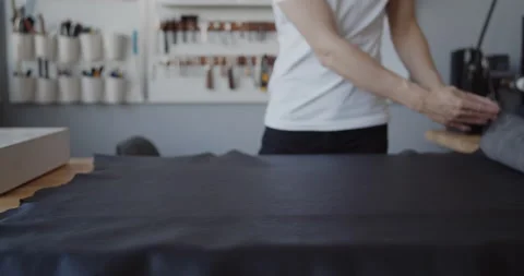 Young leather worker examining large leather piece on a table in workshop Stock Footage 144894592