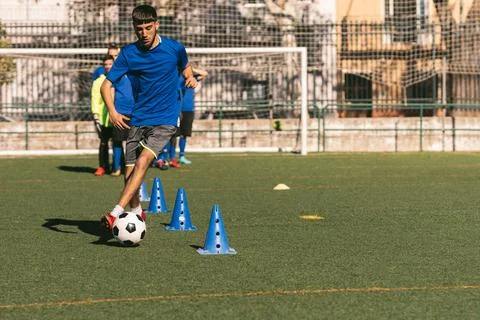 Young left-footed player dribbles cones out cones with a football Stock Photos