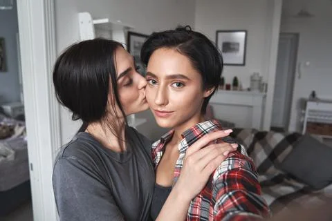 Young lesbian couple kissing taking selfie at home, camera view portrait. Stock Photos