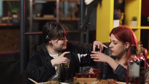 A young lesbian couple sits at a table in a bar and drinks alcoholic shots Stock Footage 251921601