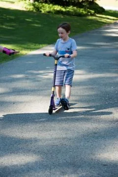 Young litte boy outside riding his scooter in the driveway Stock Photos