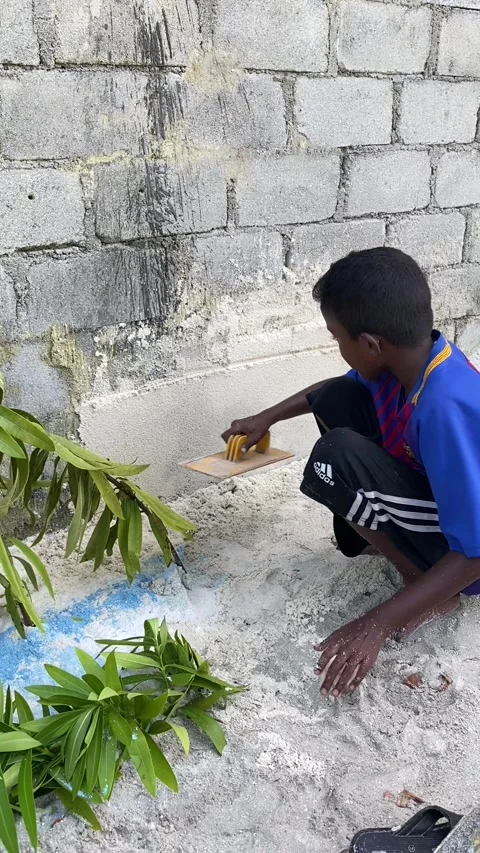 Young local boy plastering wall on sandy street Maldives vertical 库存影片 344699648