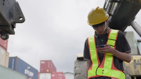 Young logistics worker in a hard hat uses a smartphone to manage inventory and Stock Footage 334946579