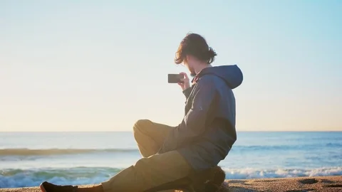 Young lonely man making picture or photo y smartphone camera sunrise sky and sea Video stock 100898647