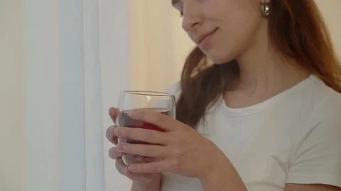 A young long-haired brunette with a cup of tea in her hands comes to the Stock Footage 234898569