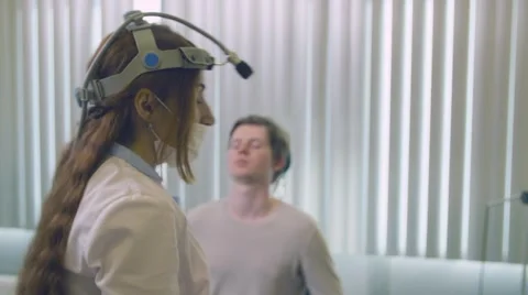 Young long-haired doctor with light on head checking man Stock Footage 62296138