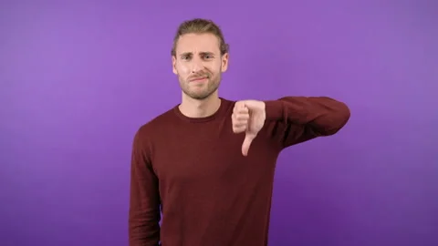 Young long-haired guy showing dislik on isolated purple background 4k Stock Footage 148830971