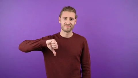 Young long-haired guy showing dislik on isolated purple background 4k Stock Footage 148831206
