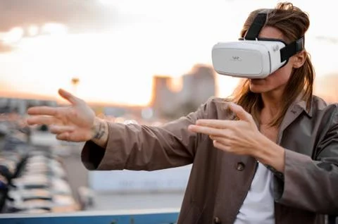 Young long-haired man enjoying VR glasses on the background of sunset Photos