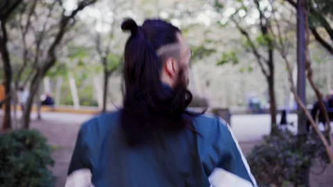 Young long-haired man exercising in a city park, wearing wireless headphones Stock Footage 155176151