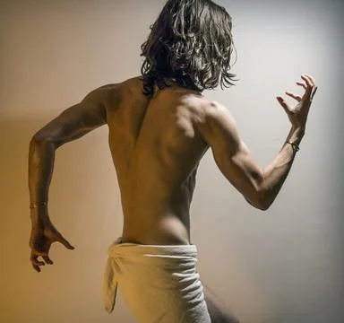 Young long haired man flexing muscles, dramatic theatrical lighting Stock Photos