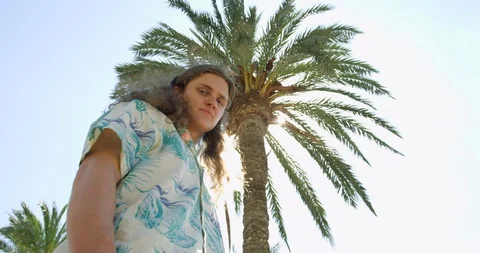 Young Long Haired Man under Spanish Palm Tree in Palma in Hawaian Hipster shirt  Stock Footage 94424904