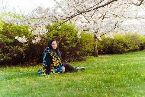 Young long-haired plus size woman sitting on grass under branches of cherry Stock Photos