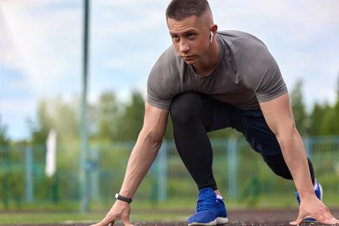 Young long-legged runner at a low start on the treadmill of the city stadium Stock Photos